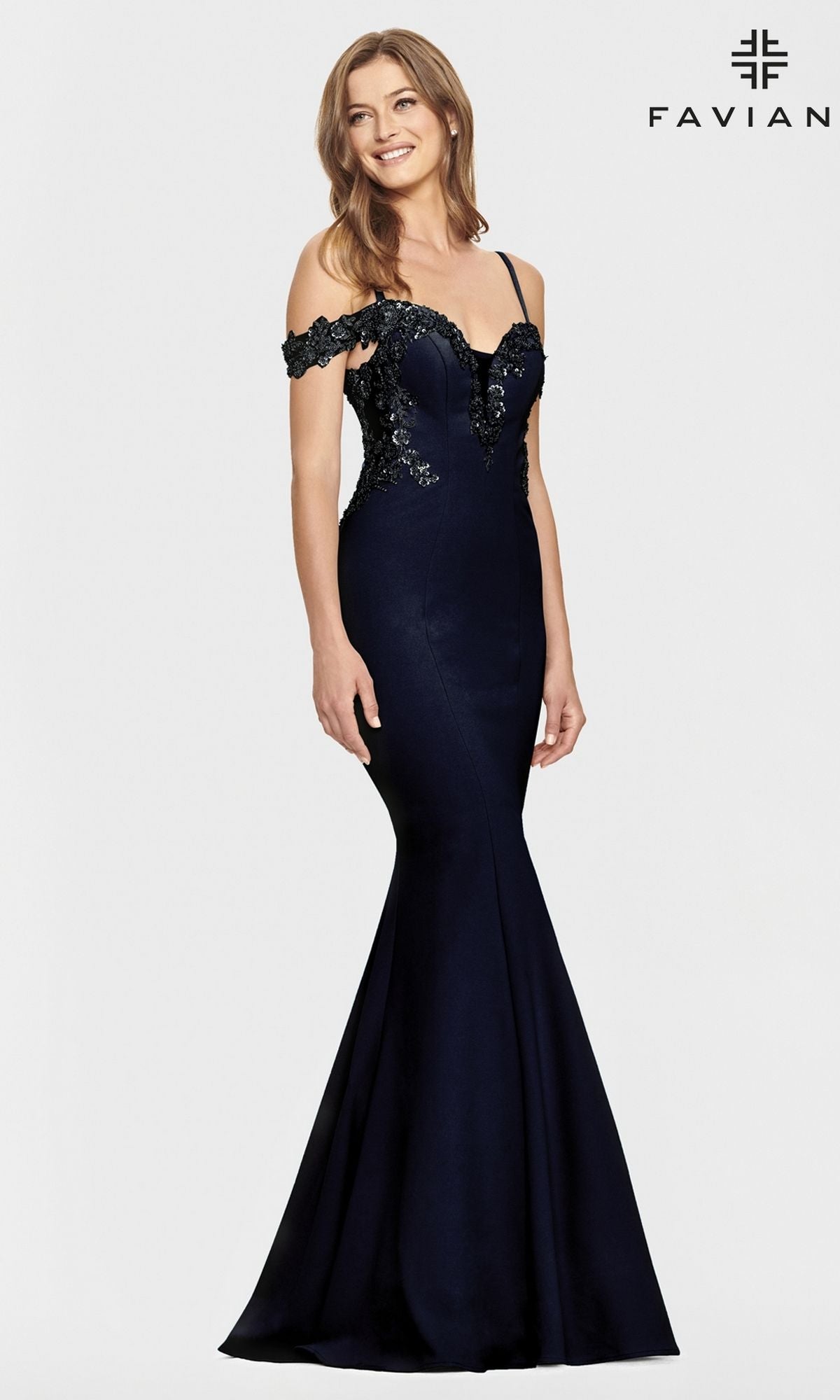 A woman stands smiling against a plain background in the Faviana Cold-Shoulder Navy Blue Prom Dress S10866, featuring a mermaid silhouette and black lace details. The word